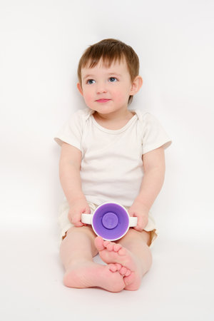 Happy baby drinks water from cup on studio white background. Resting child with cup juice in hands. Kid about two years old (one year nine months)の写真素材