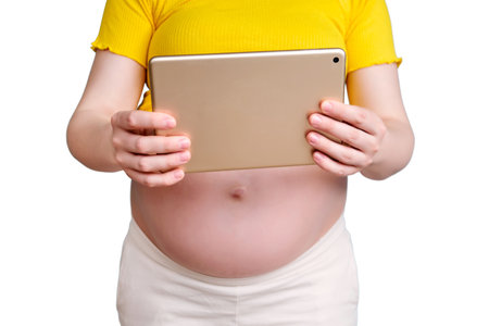 A pregnant woman holds a tablet in her hand for shooting videos and photos, isolated on a white backgroundの写真素材