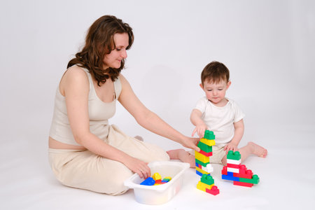 Happy baby with mother play educational toys on studio white background. Portrait of a smiling baby with mom and playing while sitting on the floor. Kid about two years old (one year nine months)の写真素材