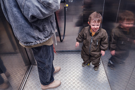 A small child rides with a woman mother in an elevator. Baby is standing with a parent in the elevator of an apartment building. Kid aged about two years (one year ten months)の写真素材