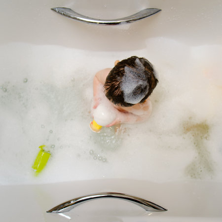 A happy child is playing with toys while sitting in a white homemade bathtub. Little toddler baby boy bathes in a bubble bath. Kid aged one year six monthsの写真素材