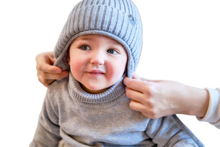 Child is dressed in warm winter clothes for a walk outside, isolated on white background. Woman mother puts clothes on toddler baby boy for cold weather. Kid age one year five monthsの写真素材