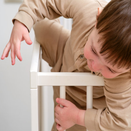 Baby escapes from the crib by climbing over the bars. The child climbs over the bed rail. Kid aged about two years (one year nine months)の写真素材