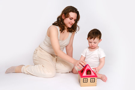 Happy baby with mother play educational toys on studio white background. Portrait of a smiling child with mom and playing while sitting on the floor. Kid about two years old (one year nine months)の写真素材