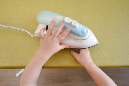 The child's careless behavior in playing with a hot iron in the living room could result in burns or injuries to the baby if left unsupervised. Kid aged about two years (one year ten months)の写真素材