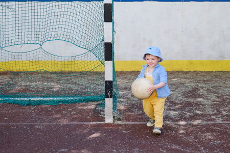 The child's happiness is evident as they run after the ball on the sports field. Baby is happily...