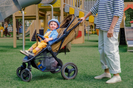 Mother with a baby boy in a pram is enjoying the sunny weather at the playground. Kid aged about two years (one year eleven months)の写真素材