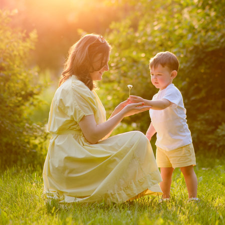 A mother woman holds a flower in her hands together with a baby in nature. Happy child with mom on a walk in the summer park. Kid aged about two years (one year eleven months)の写真素材