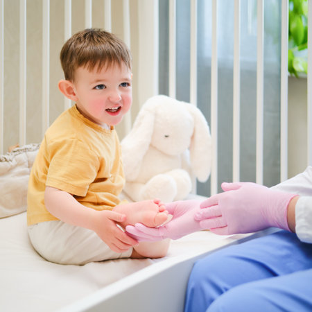 Doctor does gymnastics and foot massage to a toddler baby. Nurse in uniform doing orthopedic leg exercises to the child. Kid aged about two years (one year eleven months)の写真素材