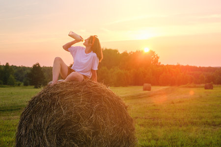 The sunrise illuminates a farm as an adult woman drinking milk in the fields during autumn. Portrait of a happy 35 year old womanの写真素材