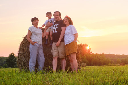 A happy family enjoys the summer evening as the father holds her baby boy in her arms, surrounded by stacks of straw in a picturesque field.の写真素材