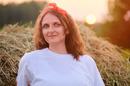 Portrait of a happy 35 year old woman. A white dress adds to the beauty of a woman standing in a field of hay bales against a sunseの写真素材