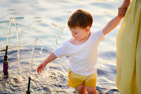 A little boy and his mom take a rest by walking in the cool waters of the fountain on a hot summer day. Kid aged about two years (one year eleven months)の写真素材