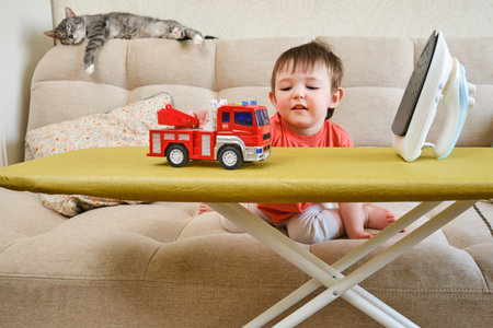 The living room is not an appropriate place for a baby to play with a hot iron without adult supervision. Children can incur serious injuries or burns if left unattended. Kid aged one year ten monthsの写真素材