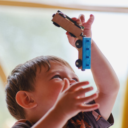 A child is playing toy cars on the background of a window. Toddler baby with a magnetic train in his...