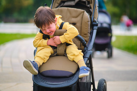 The crying baby in the stroller creates a sad expression on his face in the park. Kid aged two years...
