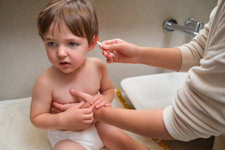 At home, a woman is taking care of her child's ear hygiene with a cotton pad in the bathroom. Kid aged two years (two-year-old boy)の写真素材