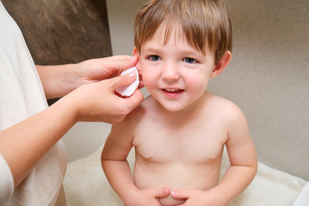 A mother is practicing good hygiene by cleaning her child ears with a cotton pad in the bathroom. Kid aged two years (two-year-old boy)の写真素材