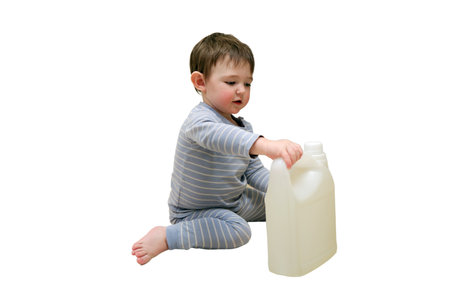 A child is playing with chemical cleaning products under the sink in the kitchen, isolated on white background. Baby holds bottles with detergent. Kid about two years (one year nine months aged)の写真素材