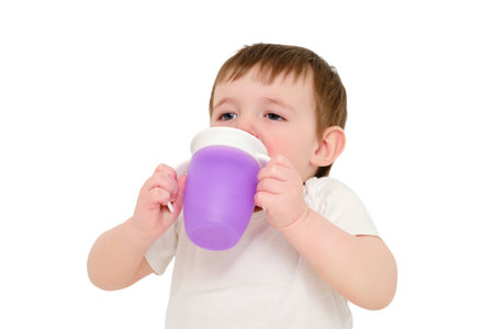 Happy baby drinks water from cup on studio, isolated on white background. Resting child with cup juice in hands, isolated on white background. Kid about two years old (one year nine months)の写真素材
