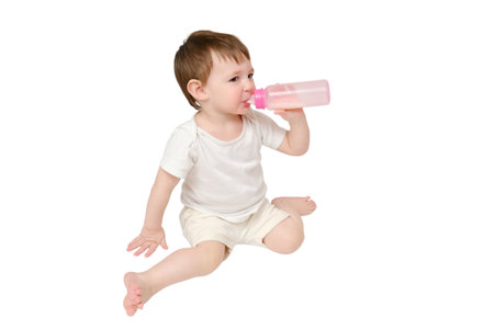 Happy baby drinks milk from bottle on studio, isolated on white background. Resting child eats formula, isolated on white background. Kid about two years old (one year nine months)の写真素材