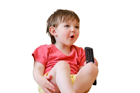 Watching cartoons on TV has brought so much happiness to the baby as they sit on the sofa with the remote control in their hand, isolated on white background. Kid aged about two yearsの写真素材
