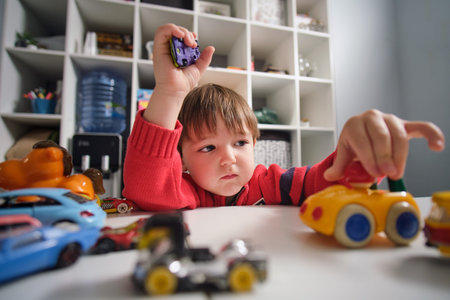 The happy baby spends his leisure time playing with toy cars at home.の写真素材