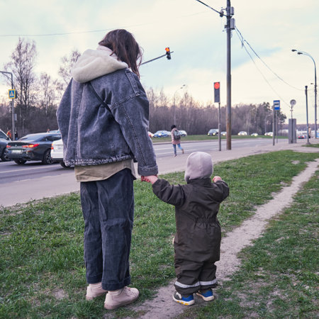 The boy and his mother walk along the city street, observing the passing cars.の写真素材