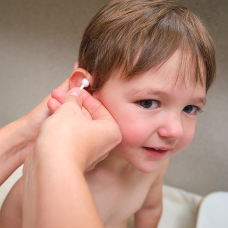 A female parent is washing her baby ears with a cotton pad in their home bathroom. Kid aged two years (two-year-old boy)の写真素材