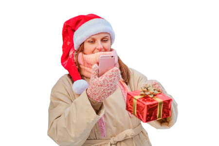 A happy woman stands with gifts and a phone in her hands at a Christmas tree in a snowy forest on New Year Eve, isolated on a white backgroundの写真素材