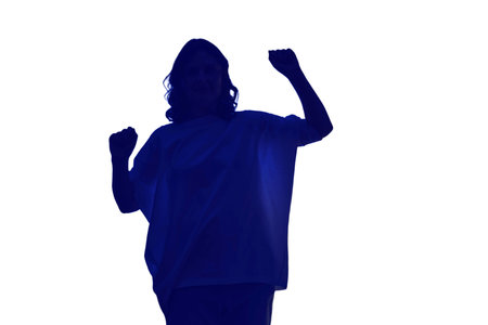 A woman is dancing near a dark window at night, low key silhouette, isolated on white background. Shadow of a female figure doing fitness against the background of a window curtain.の写真素材