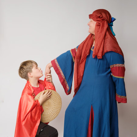 A woman in a medieval European dress and a boy bending his knee kisses her handの写真素材