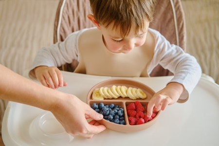 A mother woman gives her child a plate of fruits and berriesの写真素材