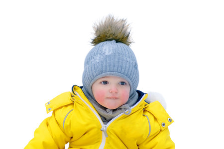 Happy toddler baby is playing with a toy in the snow in a yellow snowsuit, isolated on white background. Child boy in warm clothes walks in winter park. Kid aged one year six monthsの写真素材