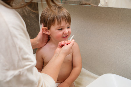 At home, the woman is washing her toddler's nose with a swab in the bathroom. Kid aged two years (two-year-old boy)の写真素材