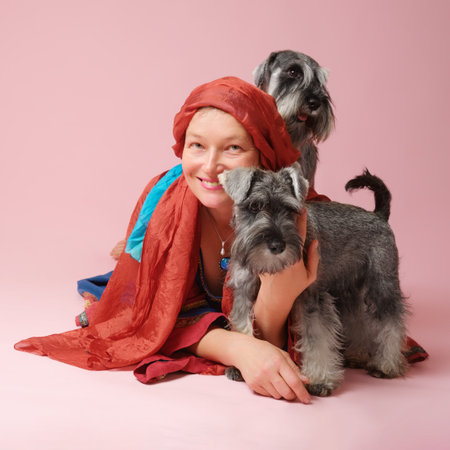 Smiling woman with two miniature schnauzer dogs on pink backgroundの写真素材