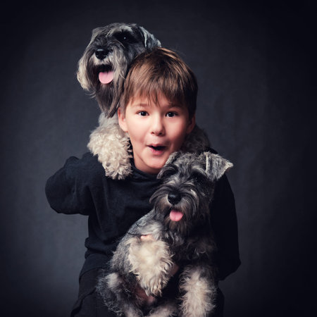 Portrait of a child with miniature schnauzer puppies. Studio shot on a dark background.