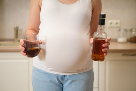A pregnant woman holds alcohol in her hands while standing in her home kitchen. Pregnancy and proper nutrition while waiting for a babyの写真素材