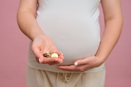 Pregnant woman holding euro cents coins in hand, studio pink background