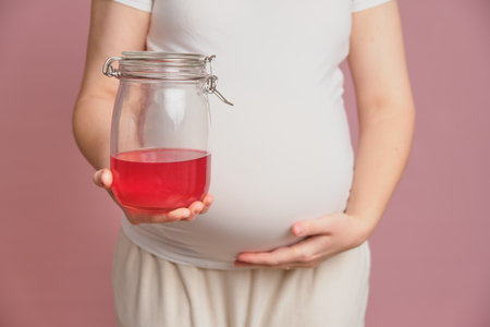 Pregnant woman holding a jar of juice in her hand, studio pink background. Concept of pregnancy and proper nutritionの写真素材