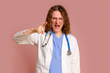 Furiously screaming female doctor, studio pink background. Nurse in uniform with stethoscope on red studio backgroundの写真素材
