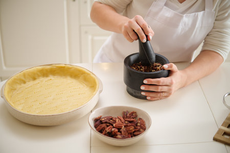 Woman using mortar and pestle while making pecan pie. Process of cooking pecan pie in home kitchen for American Thanksgiving Day.の写真素材