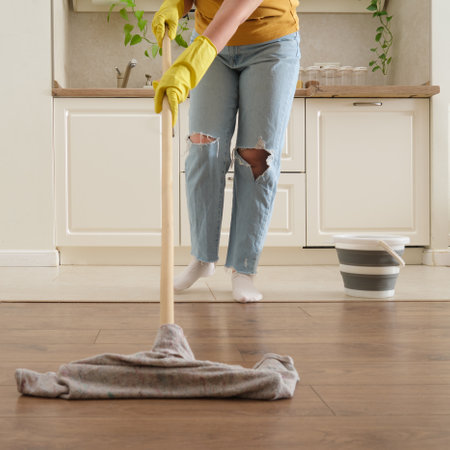 A woman mops the floor in her home kitchen. Female hands in yellow gloves while cleaning the kitchenの写真素材