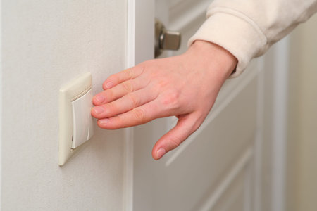A woman's hand turns on the light with an electric switch, close-up