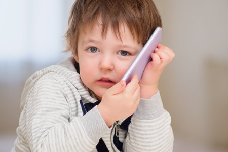 A scared baby is talking on a mobile phone. A sad child is on the phone. Kid aged two years