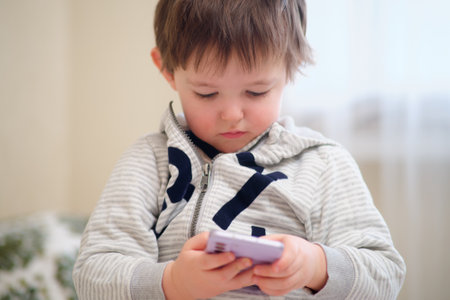 Baby plays with a mobile phone. The child looks at the phone screen. Kid aged two yearsの写真素材