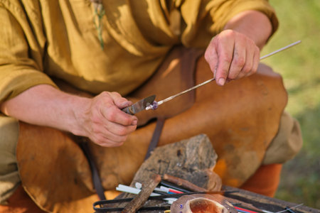 A man makes retro handmade jewelry over a fire with a knife