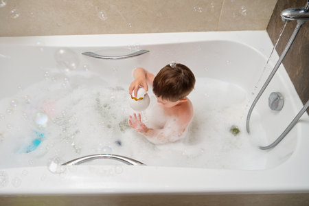 A young boy is playing in a bathtub with a toy. The bathtub is filled with bubbles and the boy is holding a white object. Kid aged 3 years (three year old child)の写真素材