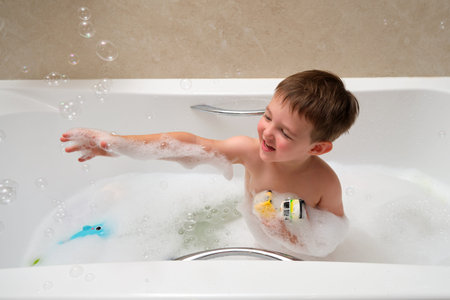 A young boy is playing in a bathtub with bubbles and a toy. He is smiling and enjoying himself. Kid...