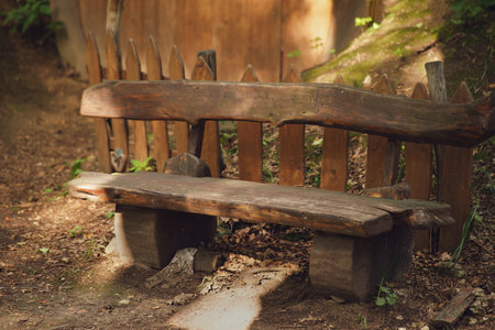 Rustic wooden bench in a wooded area with a wooden picket fence. Nature and outdoor seating concept for design and print.の写真素材